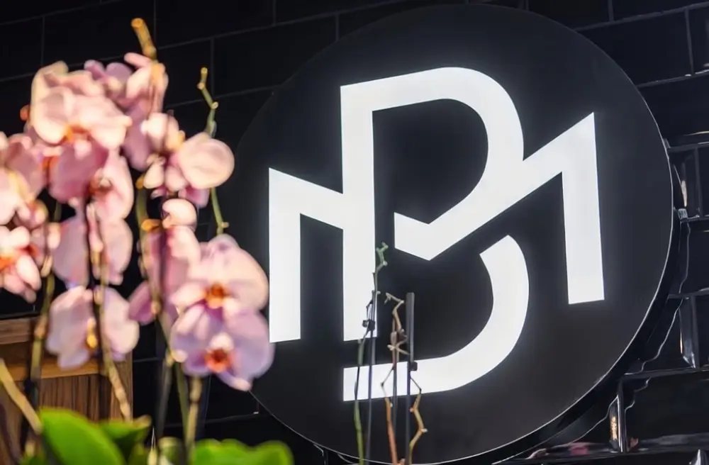 Das schwarze Leuchtschild mit dem My-Bread-Monogramm, davor rosa Orchideen