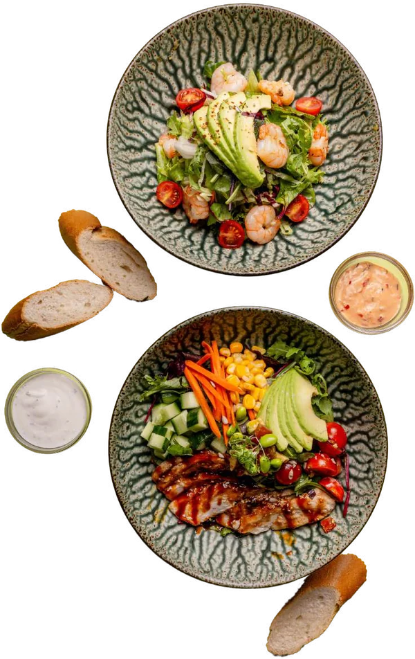 Zwei Salad Bowls mit Avocado, Cherrytomaten, Sprossen und Baguette